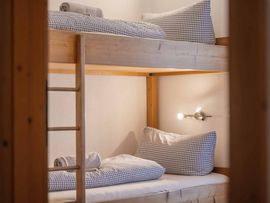 Gemütlicher Schlafraum mit einem Etagenbett aus hellem Holz. Die Betten sind mit karierten Bettdecken und Kissen sowie zusammengerollten Handtüchern ausgestattet.