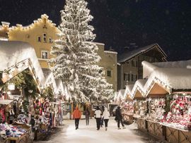 Weihnachtsmarkt in Sterzing mit hell erleuchtetem Weihnachtsbaum und Hütten.