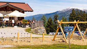 Bergrestaurant mit Terrasse, Spielplatz und Mountaincart-Startplatz vor einer alpinen Landschaft.