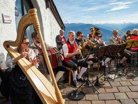 Musikgruppe spielt vor einer Bergkulisse auf einer Terrasse.