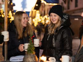 Eine Gruppe von Freunden stößt mit Glühwein an einem Stand auf dem Weihnachtsmarkt an